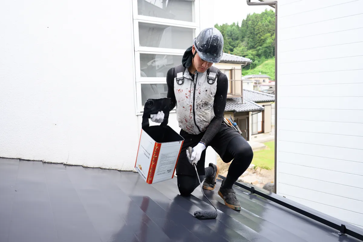 濃紺の金属屋根をローラーで塗装する有限会社マルニ工芸の職人